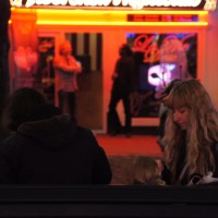 Mom feeding her tiny baby on a bench in front of a strip club.