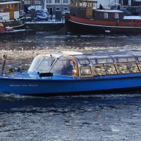 Tour boat crashing through the frozen Amstel river at the Prinsengracht